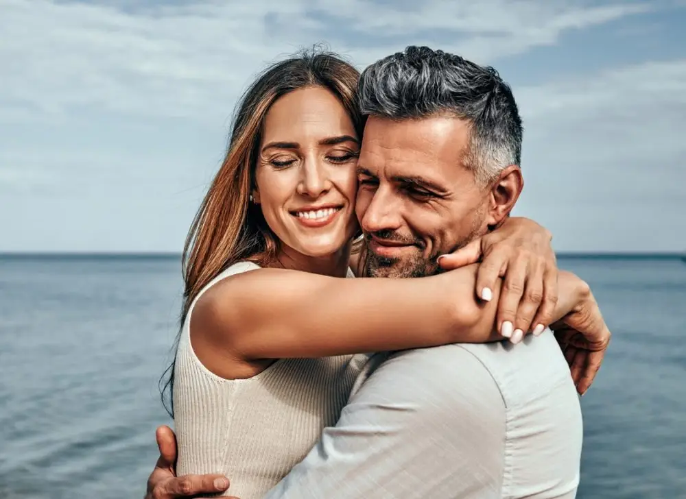 Close up view of a portrait of a handsome couple in love hugging while walking along the beach