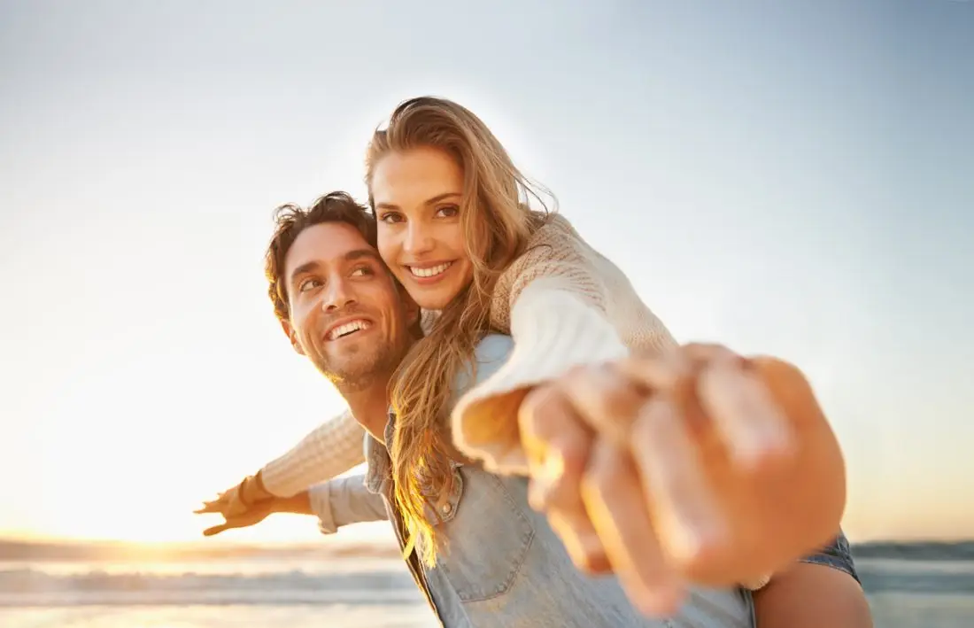 A loving young couple standing on the beach with their arms outstretched and holding hands